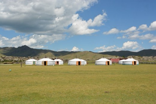 White guest gers of a tourist camp on open grassland below hills in Övörkhangai